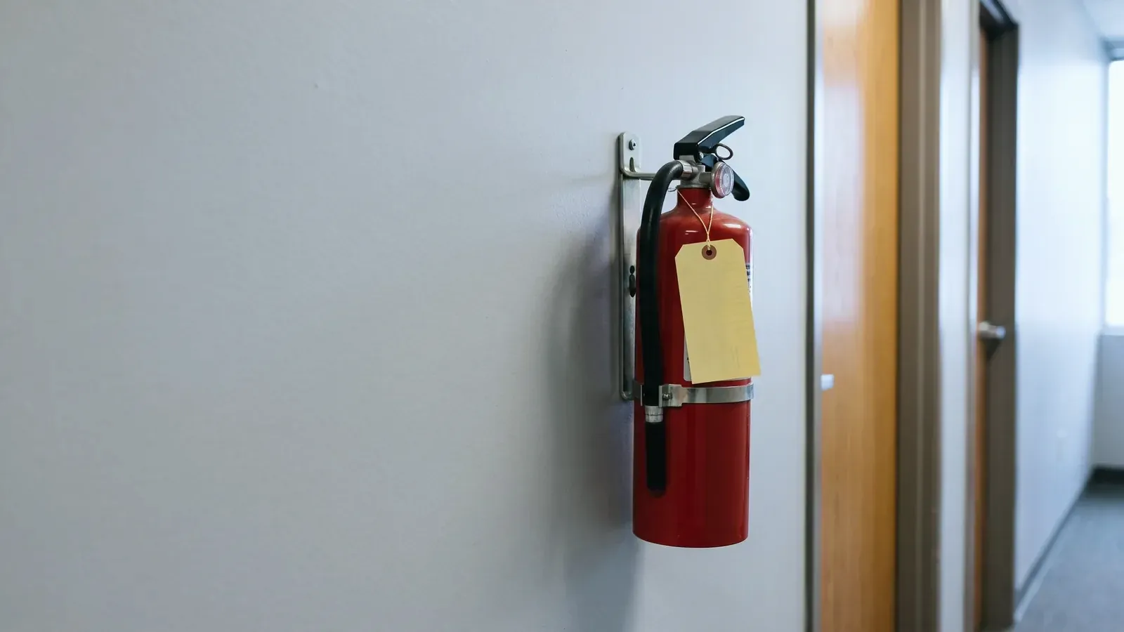 Wall-mounted fire extinguisher with a yearly inspection tag in an office corridor